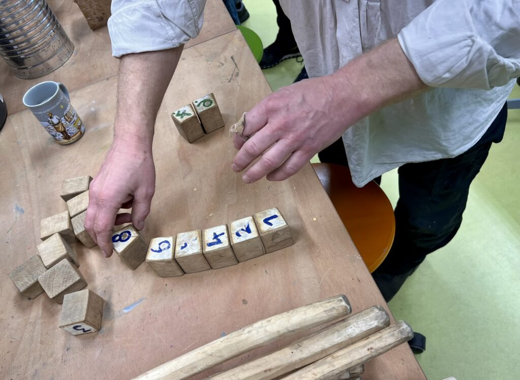 An einem Tisch legt eine Person einen Bogen aus Holzklötzchen mit den Ziffern 1 bis6.